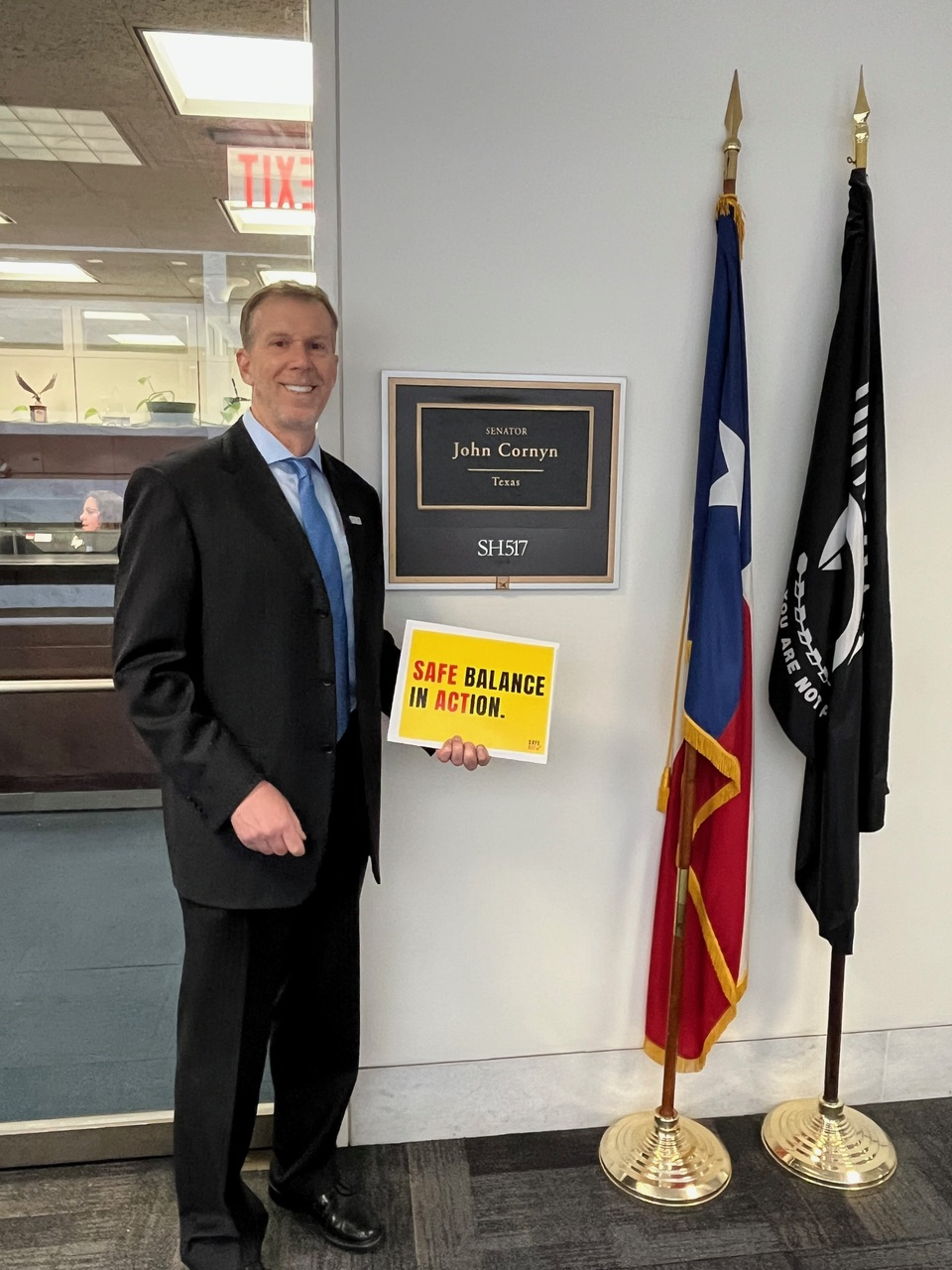 Chris Reading holding a bright yellow sign that says SAFE Balance in ACTION with the words SAFE and ACT in the color red.