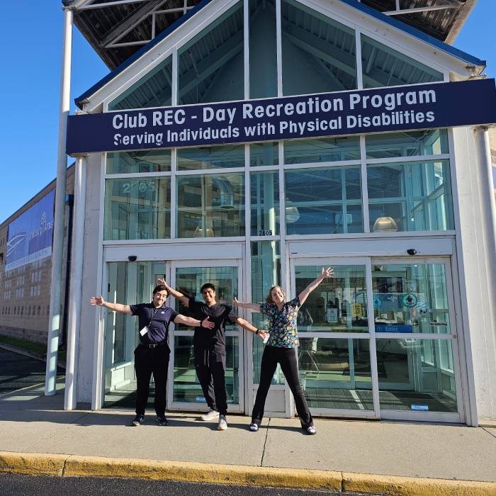Students standing outside building under sign Club REC - Day Recreation Program Serving Individuals with Physical Disabilities